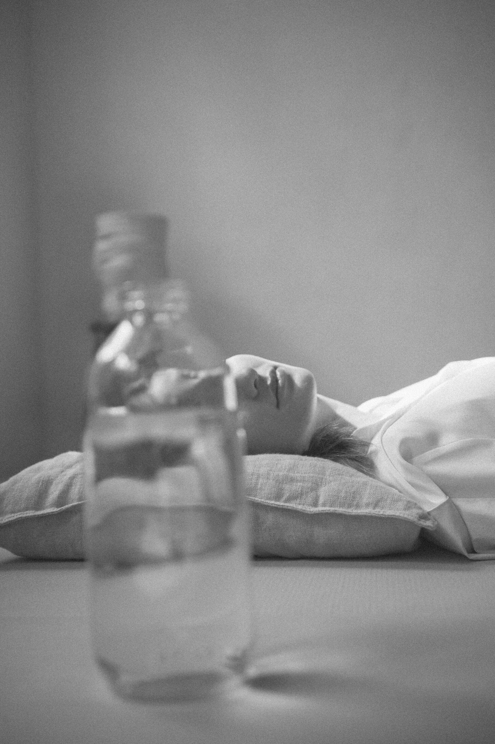 Woman lying on bed, face hidden by bottle.